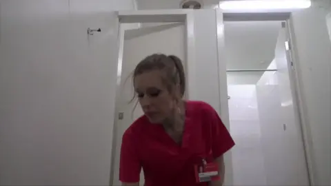 Blonde nurse in red scrubs locked in chastity and shackles
