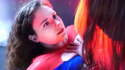 Brunette in red outfit gets touched by gloved hand on floor
