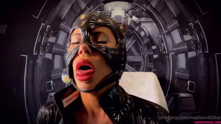 Black curvy femme in leather catsuit poses with drink in dim futuristi